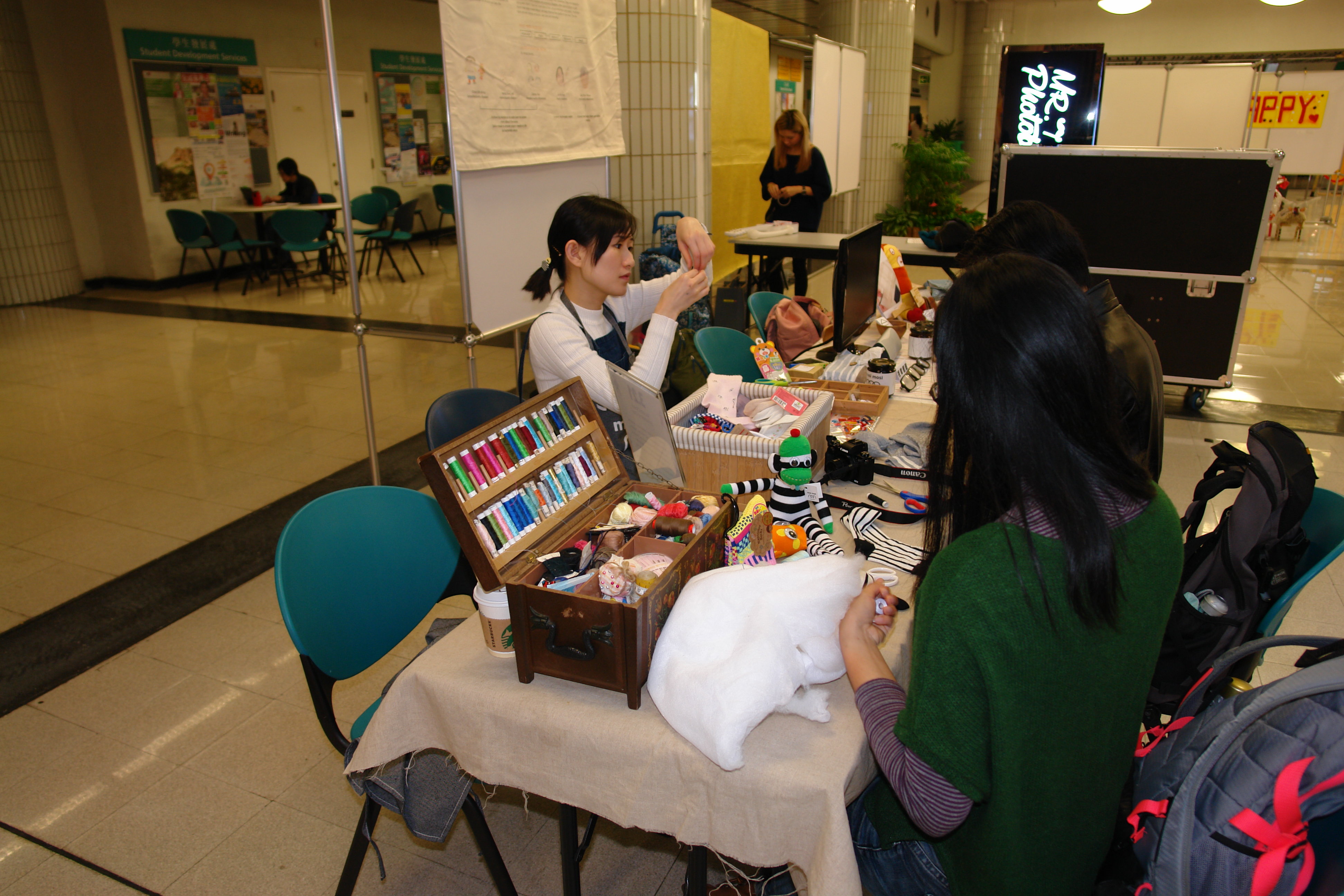 This was a sewing booth held by a lady. Tools were offered and there were participants trying to stitch patterns and clothes onto a soft toy. 